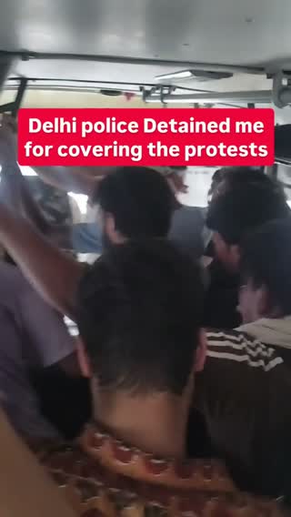 Still from the clip: several people seated inside a police vehicle, with an overlaid caption from a journalist saying they were detained for covering the protests.