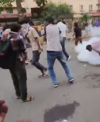 Still from the clip: people running away from a white cloud of gas on a street.